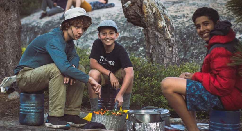 three young people use camping stoves to prepare food on an outward bound expedition 